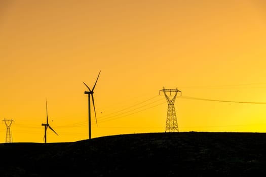 Multiple wind turbines standing on a hill at sunset and generating electricity