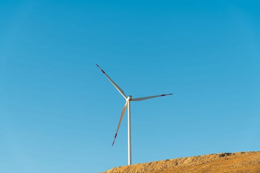 Wind turbine standing on a hill and generating electricity at sunrise