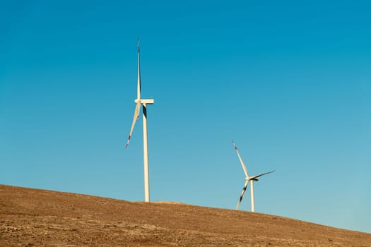 Multiple wind turbines standing on a hill at sunrise and generating electricity