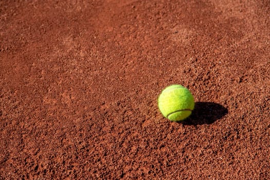 Tennis ball standing on clay tennis court on a sunny day