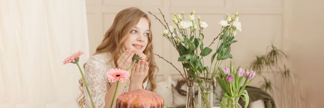 A girl with long hair in a light dress is sitting at the Easter table with cakes, spring flowers and quail eggs. Happy Easter celebration