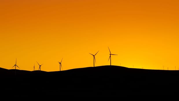 Multiple wind turbines standing on a hill at sunset and generating electricity