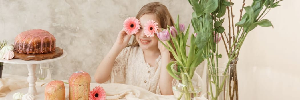 A girl with long hair in a light dress is sitting at the Easter table with cakes, spring flowers and quail eggs. Happy Easter celebration