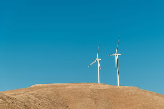 Multiple wind turbines standing on a hill at sunrise and generating electricity