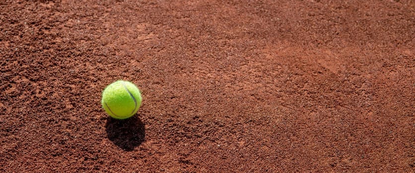 Tennis ball standing on clay tennis court on a sunny day