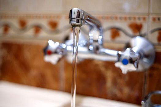 Water runs from a tap into a kitchen sink. Close up.