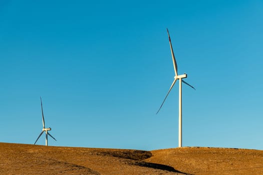 Multiple wind turbines standing on a hill at sunrise and generating electricity