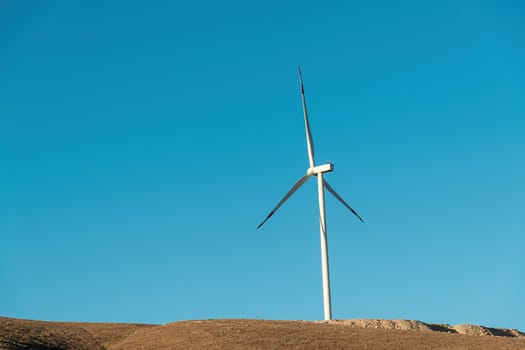 Wind turbine standing on a hill and generating electricity at sunrise