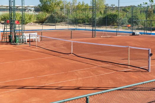 Baseline and net of an empty clay tennis court on a sunny day