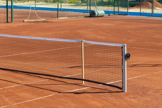 Baseline and net of an empty clay tennis court on a sunny day