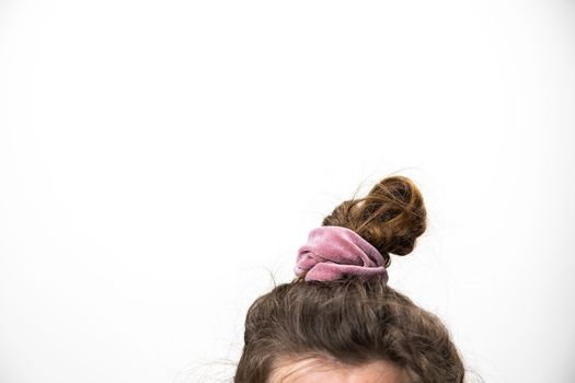 Messy hair bun female brunette closeup with grey white background and copy space, A disheveled bunch on the head of a dark-haired woman. The hair is tied with a pink elastic band. Modern fast hairstyle copy space