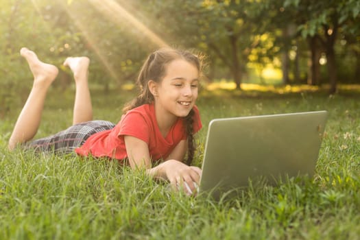 little girl usng laptop in a summer garden.