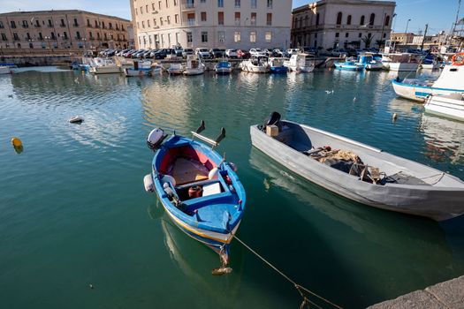 Fishing boats on the water in Ortigia island with the cityscape of Syracuse in Sicily, Italy