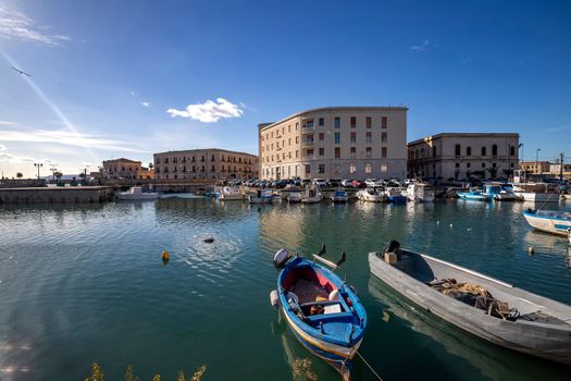 Fishing boats on water in the Ortigia island with the cityscape of Syracuse in Sicily, Italy