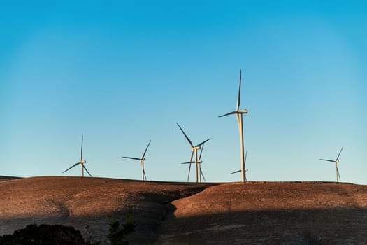 Multiple wind turbines standing on a hill at sunrise and generating electricity