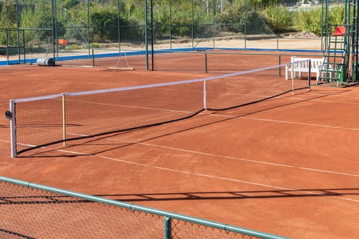 Baseline and net of an empty clay tennis court on a sunny day