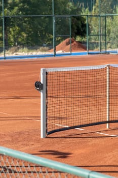 Baseline and net of an empty clay tennis court on a sunny day