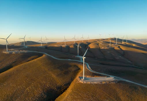 Aerial view of multiple wind turbines standing on a hill and generating electricity at sunrise