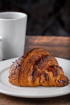 Croissant with coffee next to it on wooden table