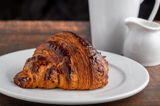Croissant with coffee next to it on wooden table