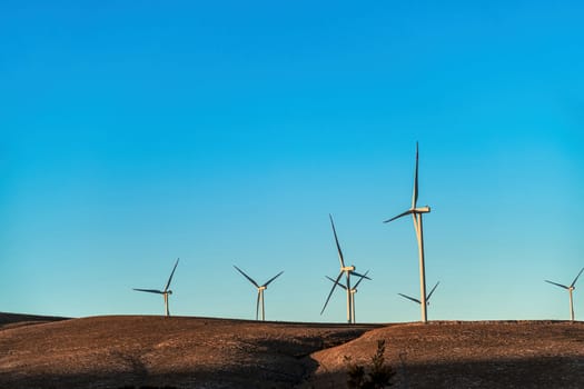 Multiple wind turbines standing on a hill at sunrise and generating electricity