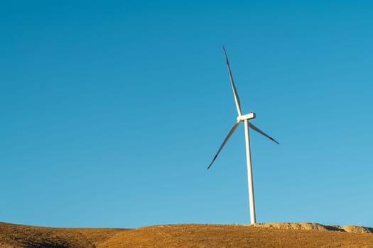 Wind turbine standing on a hill and generating electricity at sunrise