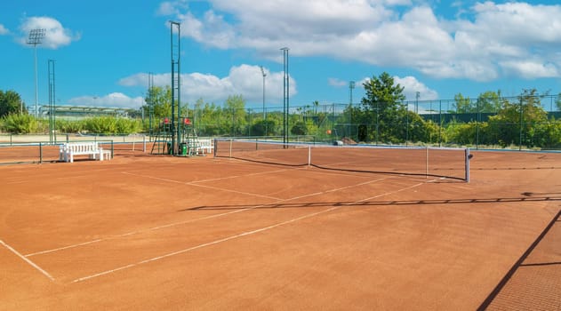 Baseline and net of an empty clay tennis court on a sunny day