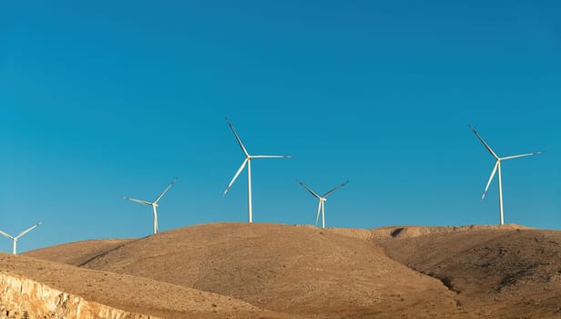 Multiple wind turbines standing on a hill at sunrise and generating electricity