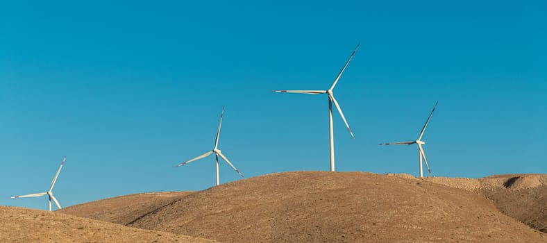 Multiple wind turbines standing on a hill at sunrise and generating electricity