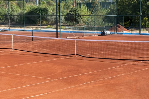 Baseline and net of an empty clay tennis court on a sunny day