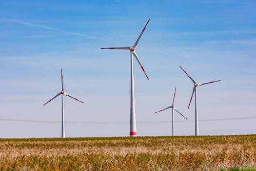 Several huge wind turbines for electricity production with fields in the foreground