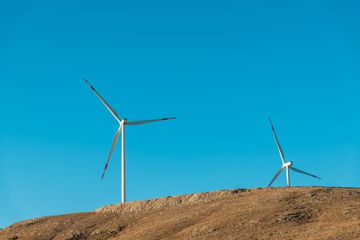 Multiple wind turbines standing on a hill at sunrise and generating electricity