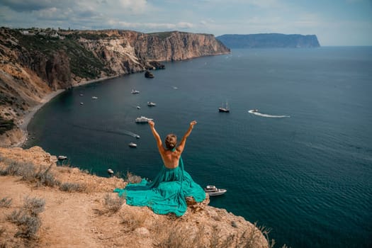 Woman sea. A happy girl is sitting with her back to the viewer in a mint dress on top of a mountain against the background of the ocean and rocks in the sea