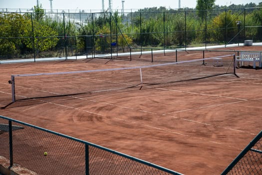 Baseline and net of an empty clay tennis court on a sunny day