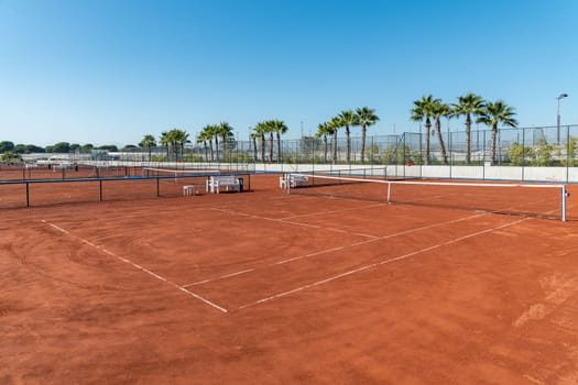 Baseline and net of an empty clay tennis court on a sunny day