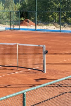 Baseline and net of an empty clay tennis court on a sunny day