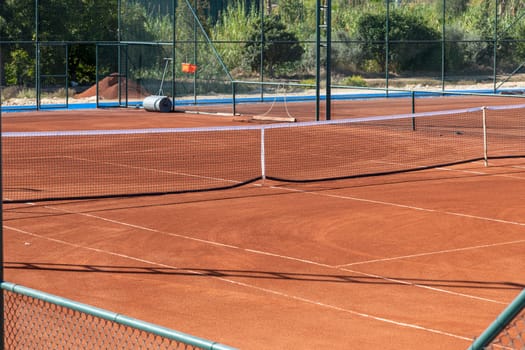 Baseline and net of an empty clay tennis court on a sunny day