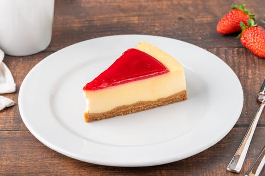 Delicious strawberry cheesecake with coffee next to it on wooden table