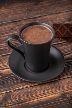 Hot chocolate in a black porcelain cup with a chocolate bar next to it