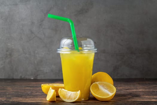 Lemonade in a take away glass with cut lemon next to it on wooden table