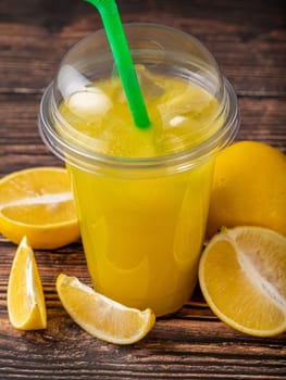 Lemonade in a take away glass with cut lemon next to it on wooden table