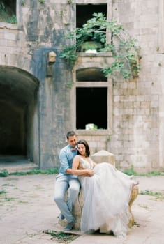 Bride and groom are sitting on a stone in the courtyard of the old fortress. High quality photo