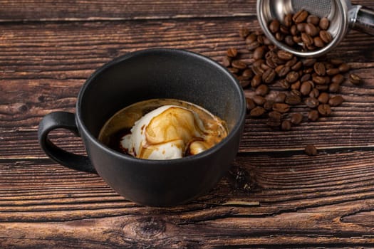 Espresso with ice cream in black porcelain cup on wooden table. Affogato Coffee