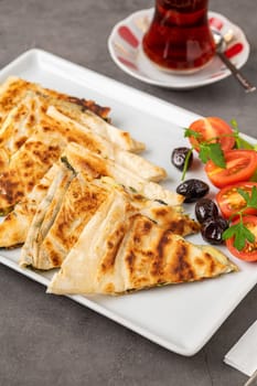 Traditional Turkish flatbread or Gozleme with tomatoes, olives and tea on dark stone table