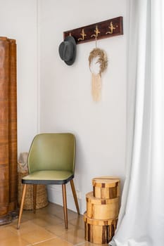 Entrance hall with white hay in atmospheric boho style. On the wall there is a carved hanger for outerwear and a man's black hat. Nice green wooden chair. Boxes on the floor for decoration