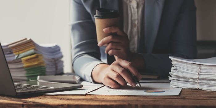 Annual, summary report, laptop and paper placed at office desk. Person back view of Asian woman work online and plan financial data with laptop, work from home. Business woman and planner concept..