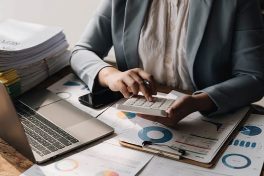 Business woman using calculator to calculate financial report, working at office with laptop computer on table. Asian female accountant or banker making calculations. finances and economy concept..