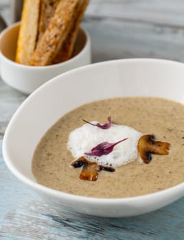 Cream of mushroom soup in white porcelain bowl on wooden table