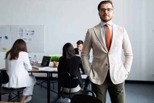 adult caucasian businessman stands against the background of working employees in the office.