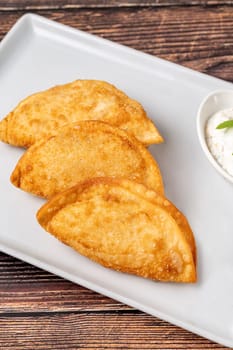 Beef Cheburek on a wooden table. Deep Fried Beef Dumplings with meat and onions. Turkish name Ci Borek or Cig Borek